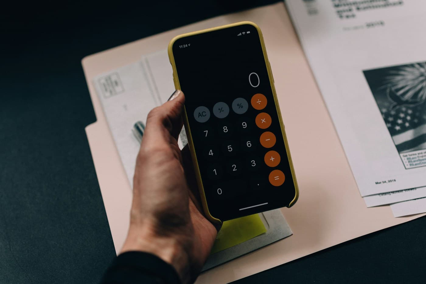 Persona usando la calculadora del celular sobre unas facturas