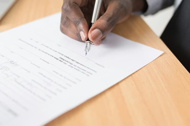 Mano firmando un documento sobre una mesa de madera